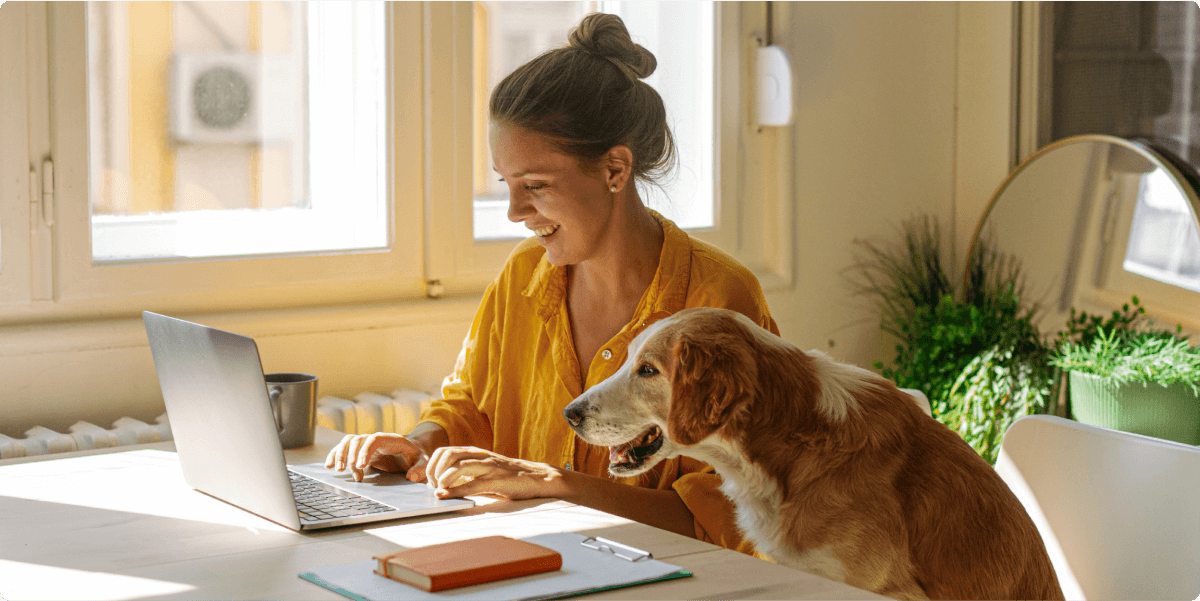 Eine Frau, die an ihrem Laptop arbeitet, mit ihrem Hund in der Nähe.