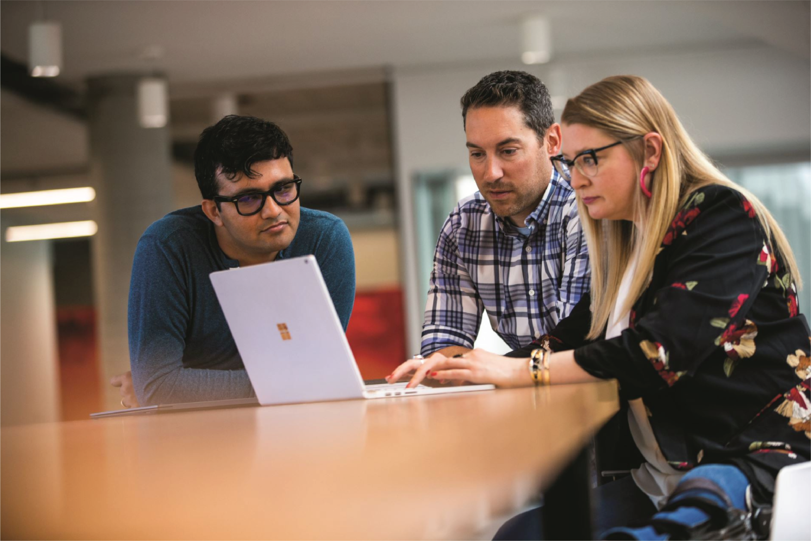 Three people sitting together at a table in front of a Microsoft Surface laptop.