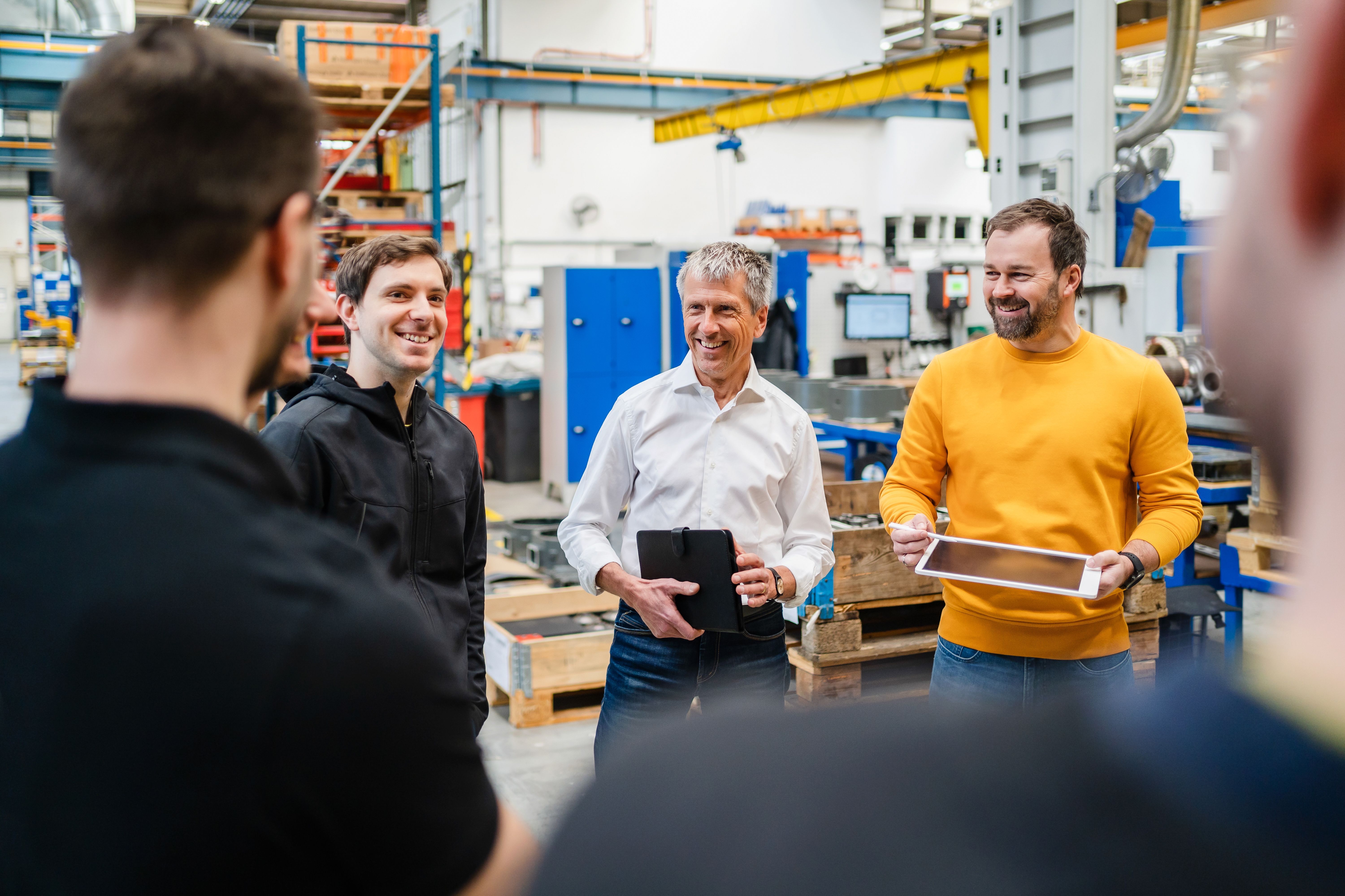 A photograph of a group standing in a circle on a manufacturing floor.