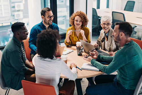 Photograph showing of people working and talking around a table.