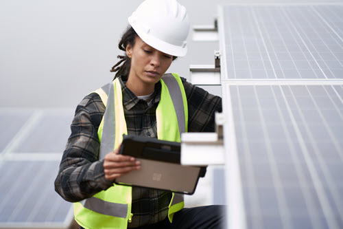 Photograph showing of person working on solar panels holding a tablet.