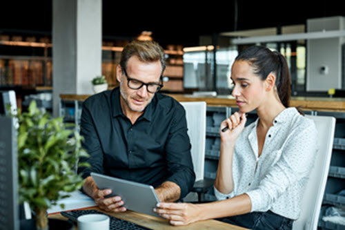 Photograph of two people looking at a tablet screen in an office.