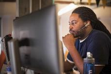 Foto di un uomo che indossa un auricolare e seduto a un computer.