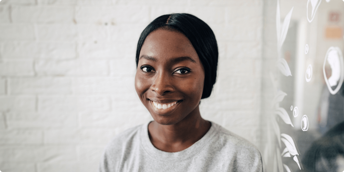 Um retrato de uma mulher sorridente em frente a uma parede de tijolos brancos.